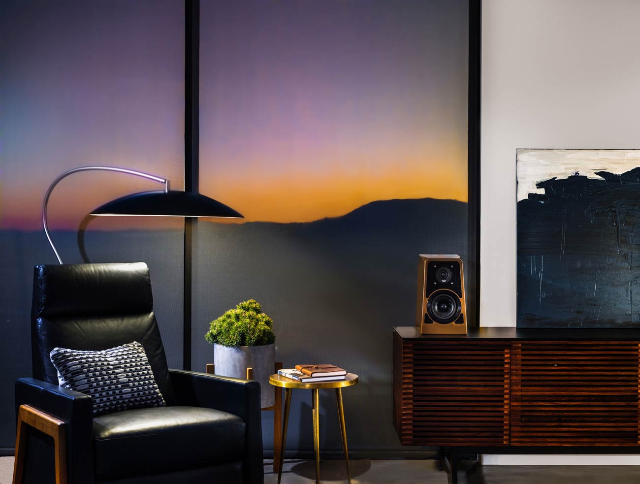 Ett elegant vardagsrum med en svart läderfåtölj, en modern lampa, en vinylhögtalare på en träkonsol och utsikt över solnedgången ger den perfekta stämningen.