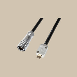 En svart MicroUSB-kabel, redo att användas - silverfärgade runda och rektangulära kontakter mot en slät beige bakgrund.