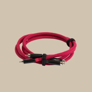 En röd Rouge RCA/XLR-ljudkabel, lindad med svarta kontakter och remmar, vilar på en enkel beige scen.