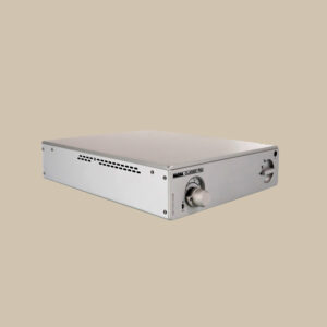 Nagra Classic PSU-förstärkare - elegant silverfärgad, med en smidig volymknapp, ventilationsöppningar på sidorna och strömbrytare - vilar på en mjuk beige bakgrund.