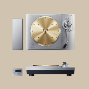 Skivspelaren SL-1000R imponerar med sin tallrik i guld och silver, sin eleganta tonarm och sina rena kontroller - musikmagi på en beige scen.
