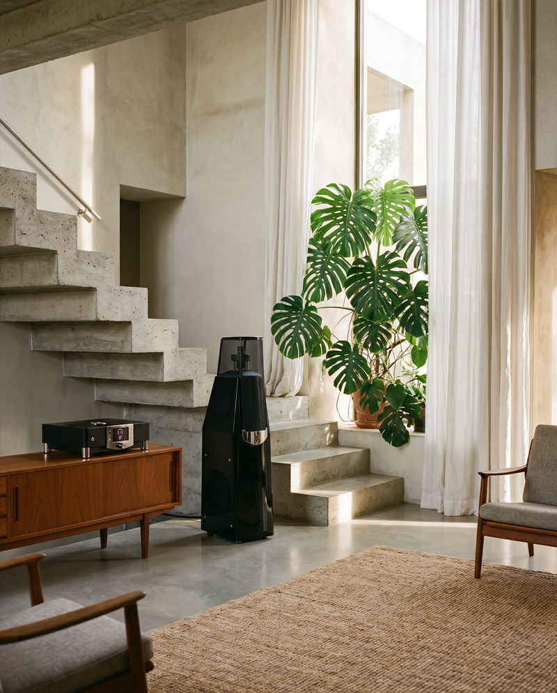 Ett modernt vardagsrum med vinylvibbar: betongtrappor, fönster med skira ljusinsläpp, monsteraplantor, träinredning och en chill minimalistisk känsla.