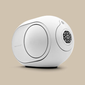 Devialet Phantom II Custom, en elegant vit oval högtalare med baselement på sidorna och ett frontgaller, står redo att rocka på en beige yta.